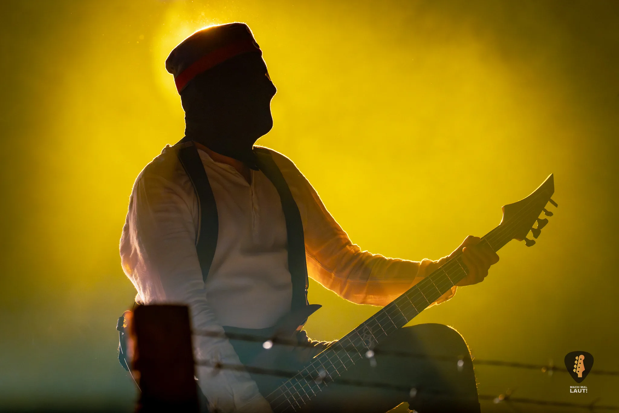 Kanonenfieber Musiker mit Maske und Gitarre vor einem nebeligen Hintergrund, der von hinten gelb angeleuchtet wird
